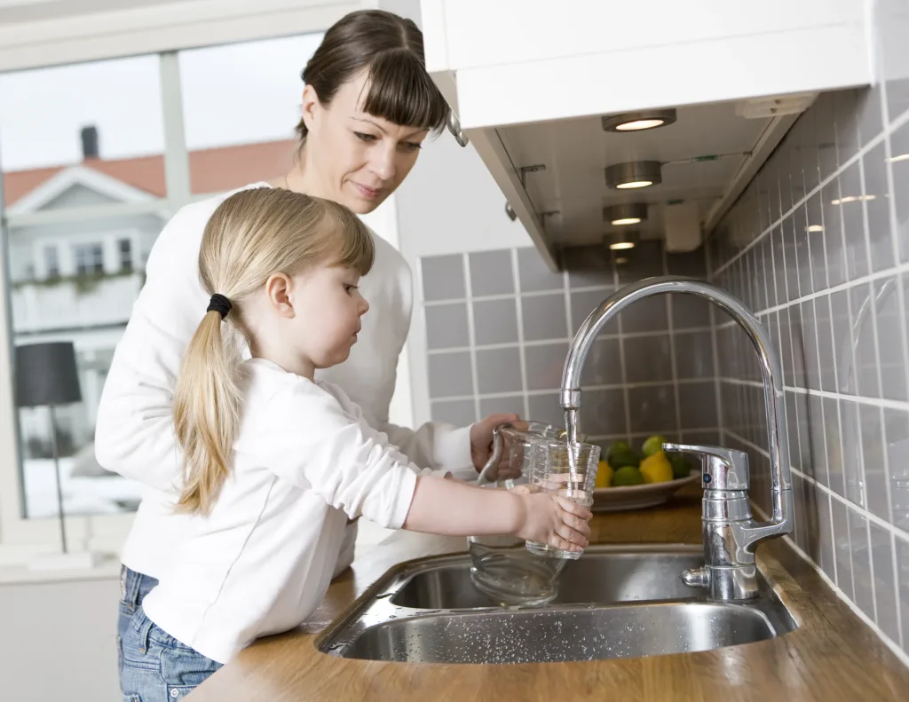 Small Girl in the kitchen with her mother drinking water